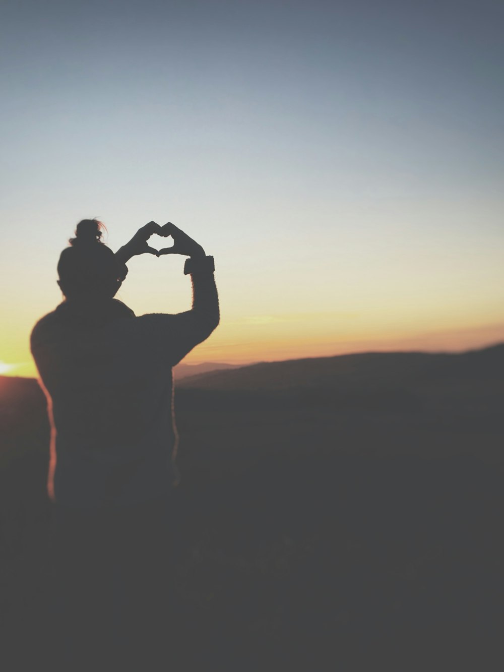 silhouette of a person making heart using her hands