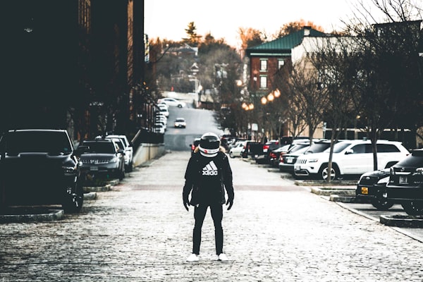 a figure dressed in black wearing a "space helmet" on a cobblestoned urban street