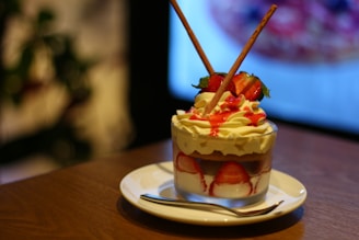 A creamy strawberry dessert topped with whipped cream and a drizzle of chocolate sauce served in a modern glass cup