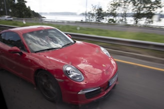 A sleek black car with red detailing driving on a scenic road.