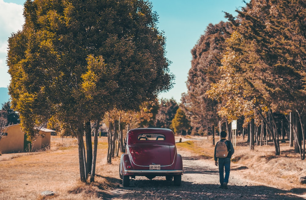 man walking beside red car