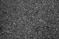 A close-up view of a rough textured asphalt surface with small stones embedded in the dark material.