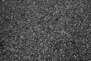 A close-up view of a rough textured asphalt surface with small stones embedded in the dark material.