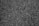 A close-up view of a rough textured asphalt surface with small stones embedded in the dark material.