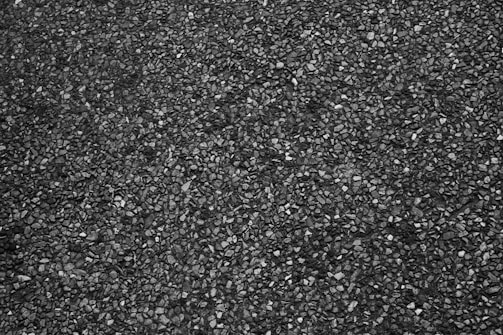 A close-up view of a rough textured asphalt surface with small stones embedded in the dark material.