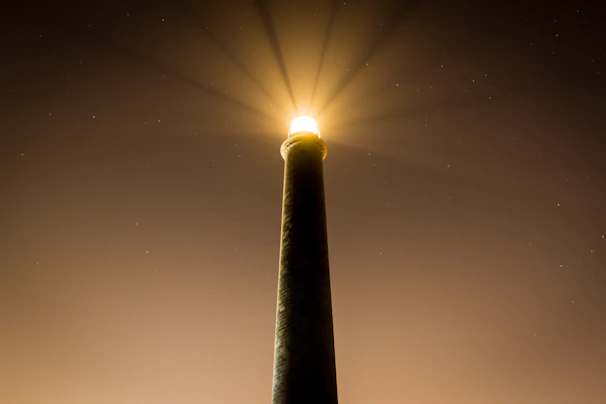 A golden lighthouse beacon illuminating a dark ocean horizon under a starry night.