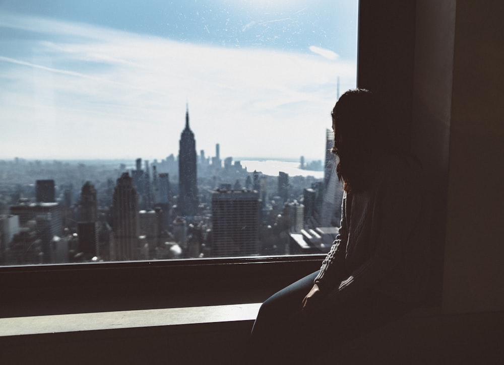 woman sitting on window edge looking at Empire State tower