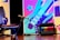 A dynamic, colorful background featuring a stylized guitar in blues and purples with abstract shapes in the background. In the foreground, there's an empty chair and a microphone on a stand, indicating a performance setting.