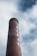 A tall brick chimney with the word 'HUMAN' painted vertically on its side. The chimney rises against a backdrop of cloudy sky, creating a striking contrast between the industrial structure and nature.
