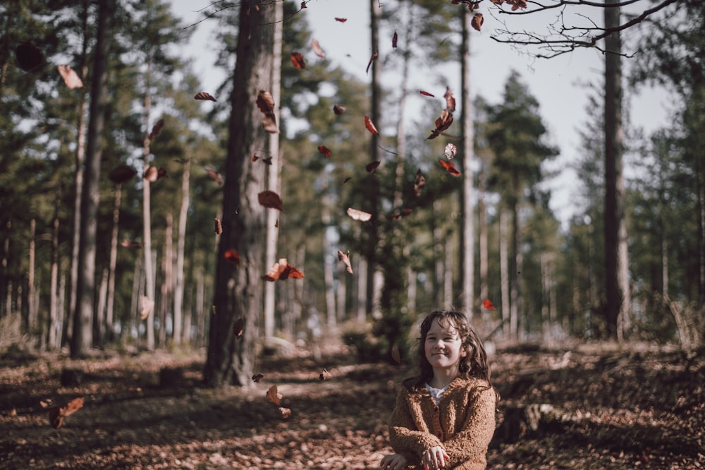 girl wearing brown jacket looking at leaves flying at daytime