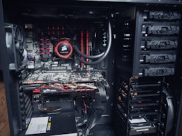 An open computer case with visible internal components, including a cooling fan, a Corsair liquid cooler, MSI graphics cards, RAM modules, and a power supply unit. The components are neatly arranged with power and data cables connected to different parts.