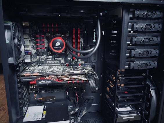 An open computer case with visible internal components, including a cooling fan, a Corsair liquid cooler, MSI graphics cards, RAM modules, and a power supply unit. The components are neatly arranged with power and data cables connected to different parts.