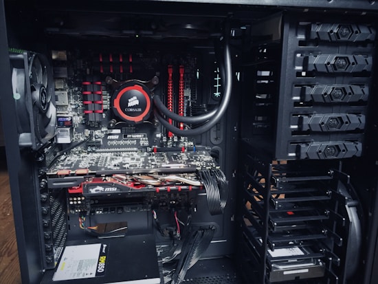 An open computer case with visible internal components, including a cooling fan, a Corsair liquid cooler, MSI graphics cards, RAM modules, and a power supply unit. The components are neatly arranged with power and data cables connected to different parts.