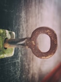 A close-up view of an old, rusty key inserted into a lock. The key and lock appear to be made of metal, with visible textures and signs of wear. The background is blurred, suggesting a shallow depth of field.