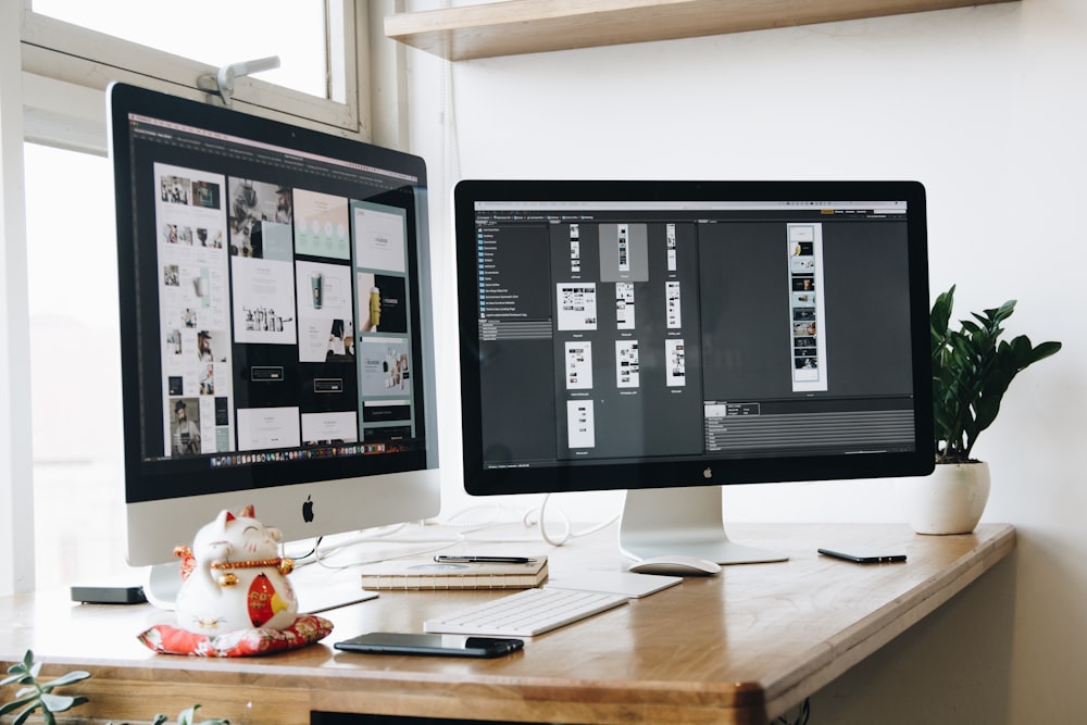 two computer monitors sitting on top of a wooden desk