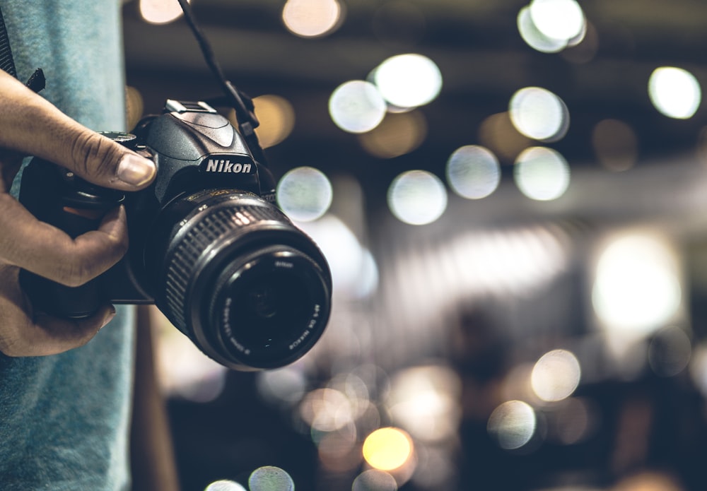 bokeh photography of person holding Nikon DSLR camera with strap