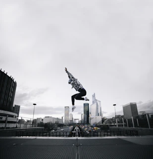 Male athlete mid-air performing a parkour jump over urban obstacles with cityscape background.