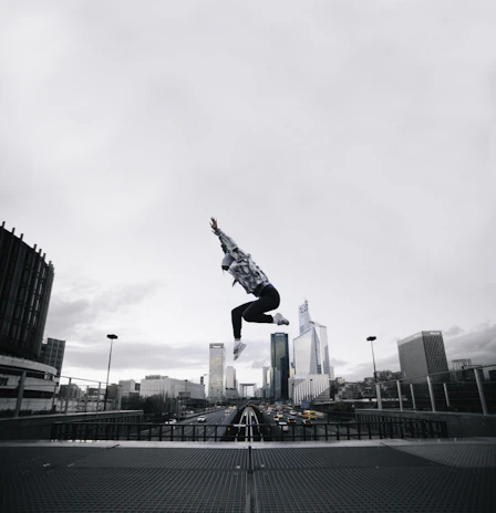 Male athlete mid-air performing a parkour jump over urban obstacles with cityscape background.