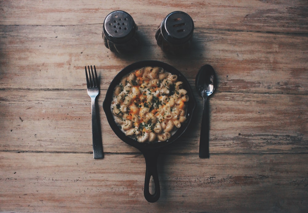 cooked food on black plate beside fork and spoon on brown wooden table