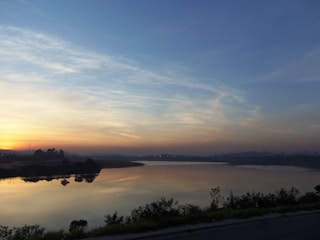 A peaceful lakeside scene at dawn with soft light blue tones reflecting on calm water.
