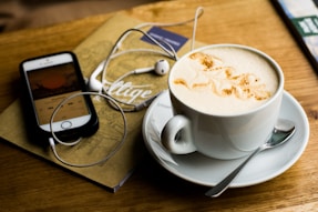 leaf design coffee latte on mug, near a music device and earbuds