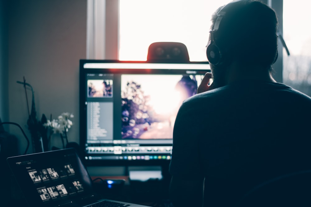 A business man working in front of a desktop monitor, laptop screen and his phone