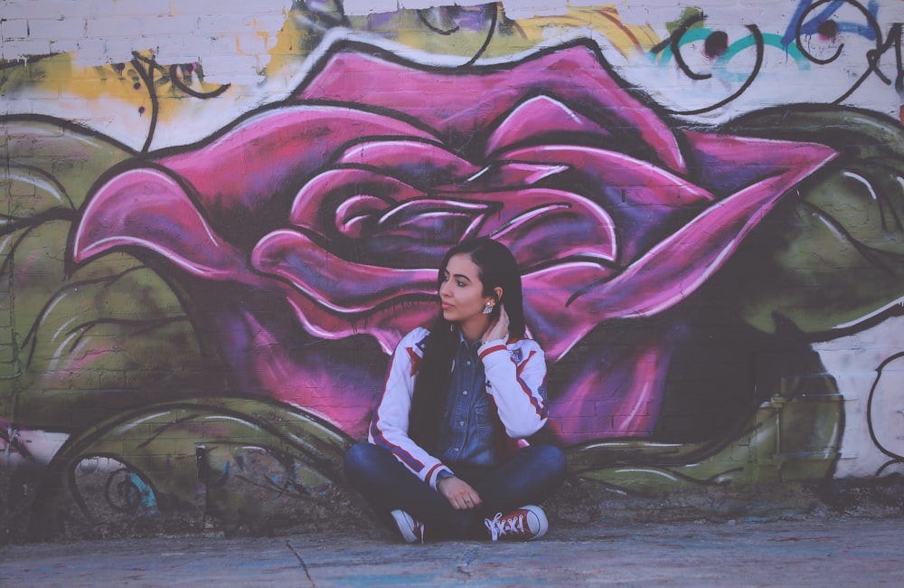 Donna che si siede accanto alla pittura murale del fiore viola