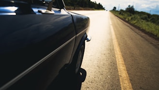 A vibrant road trip scene with a vintage car cruising along an open highway under a bright blue sky.