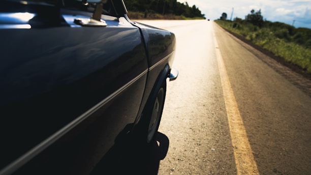 A vibrant road trip scene with a vintage car cruising along an open highway under a bright blue sky.
