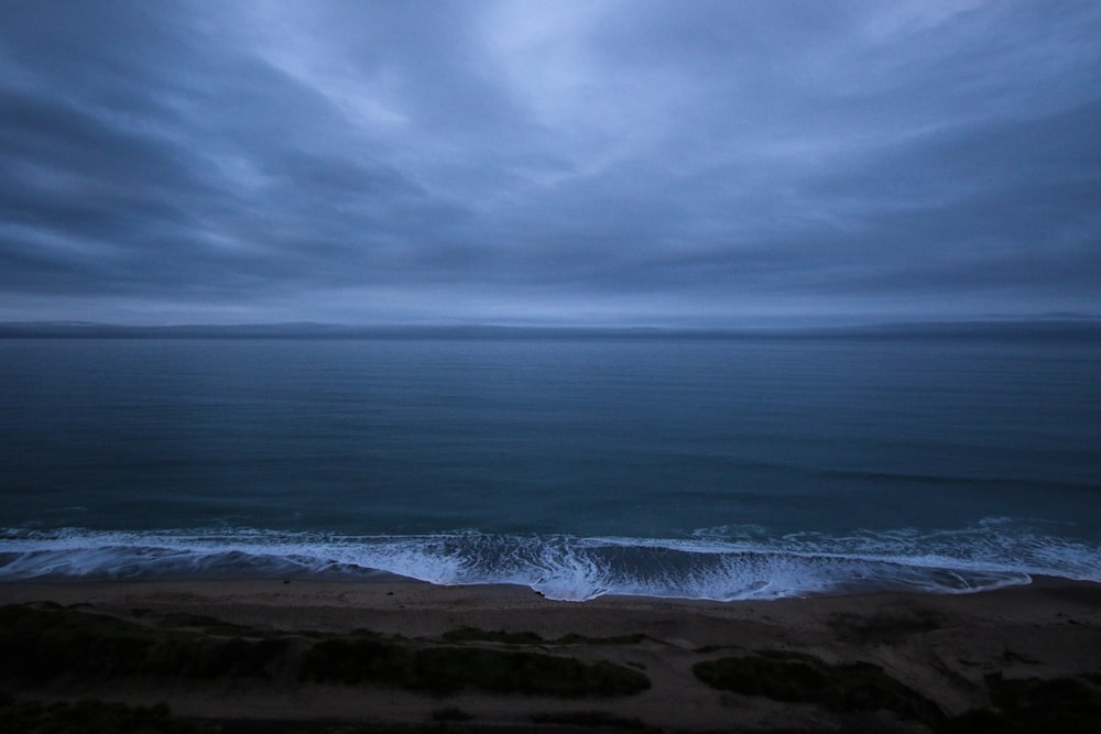 Onde dell'oceano che si infrangono sulla riva sotto il cielo nuvoloso durante il giorno