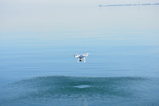 A sleek drone hovering over a serene blue lake reflecting the sky.