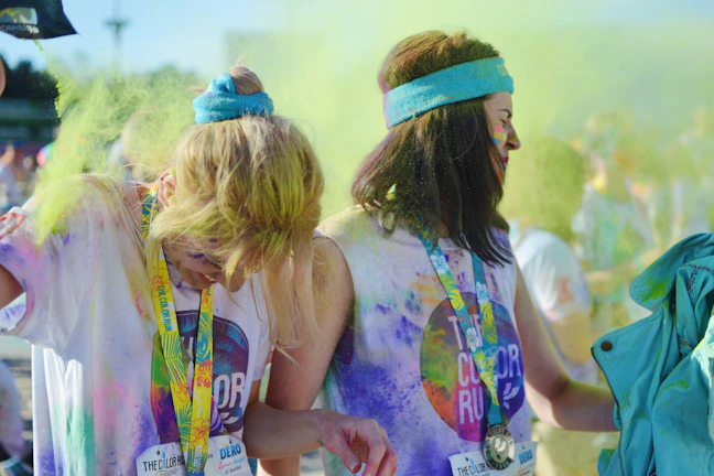 A group of happy runners covered in pink and blue powder, smiling and celebrating during the race.