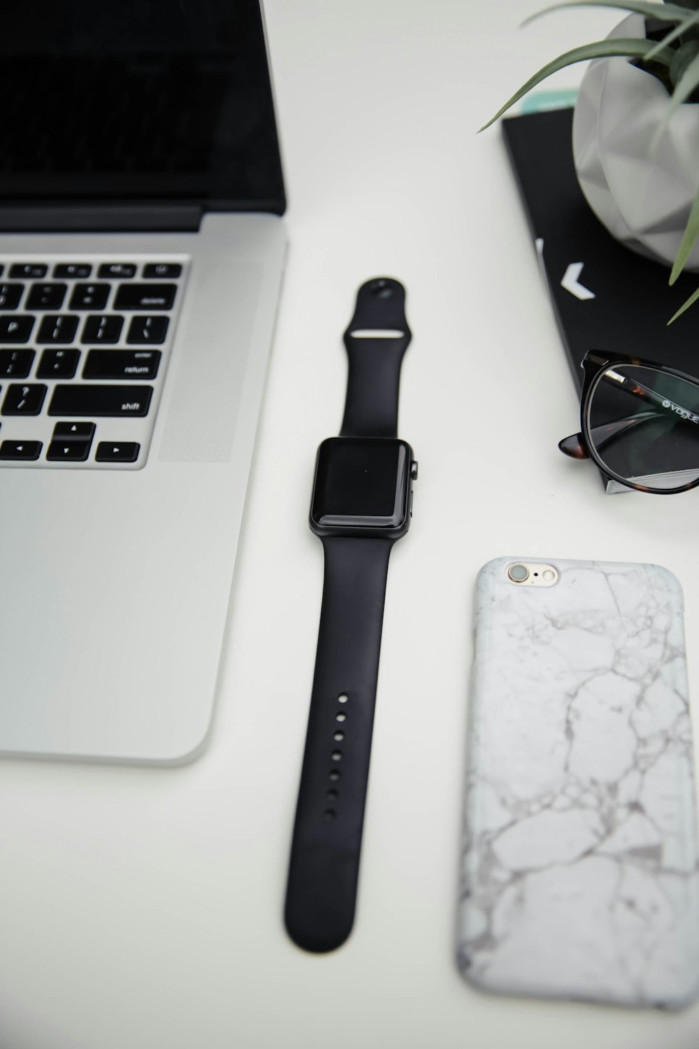 um Apple Watch, um celular e um laptop em uma mesa