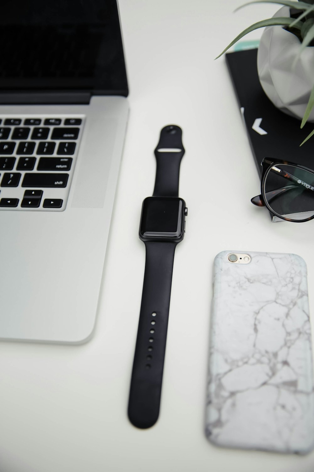 Eine Apple Watch, ein Handy und ein Laptop auf einem Schreibtisch