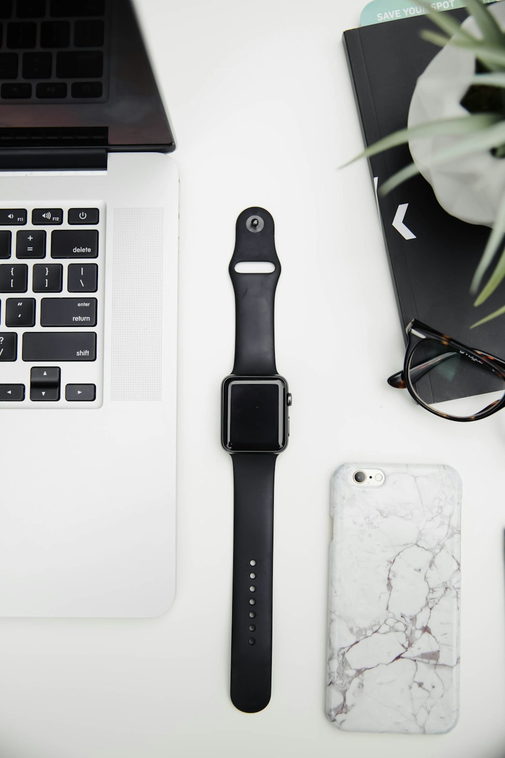 um relógio da maçã, um telefone celular e um laptop em uma mesa