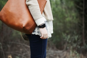 A person elegantly holding a leather bag while walking outdoors.