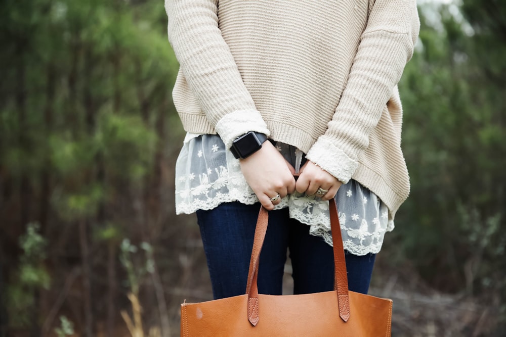 mulher em pé segurando uma sacola de couro marrom