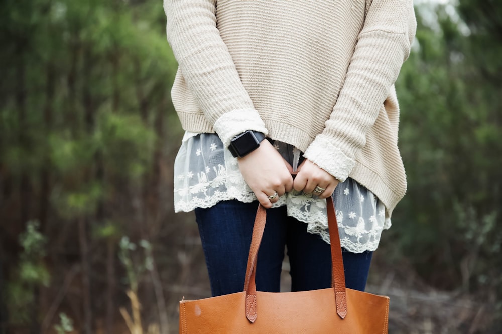 Frau steht mit einer braunen Ledertasche in der Hand