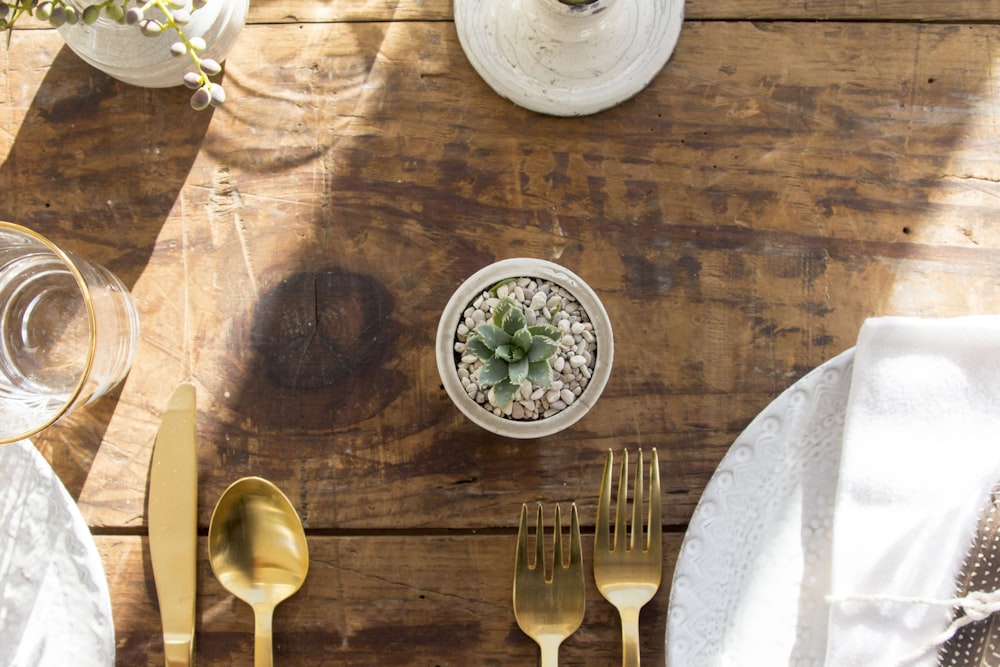 a wooden table topped with silverware and a potted plant