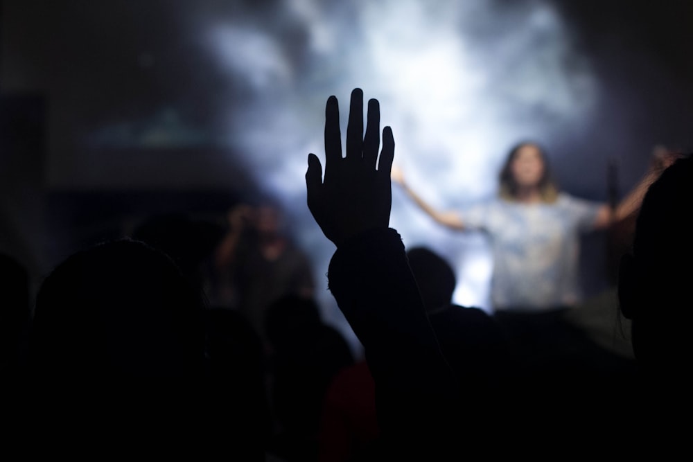 Silhouette einer Person mit rechter Hand in der Luft vor einer Frau auf der Bühne