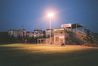 Outdoor 5v5 futsal field with teams celebrating a goal under evening lights.