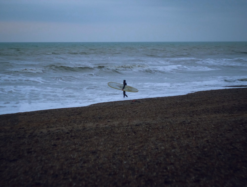 person holding white surfboard in seashore