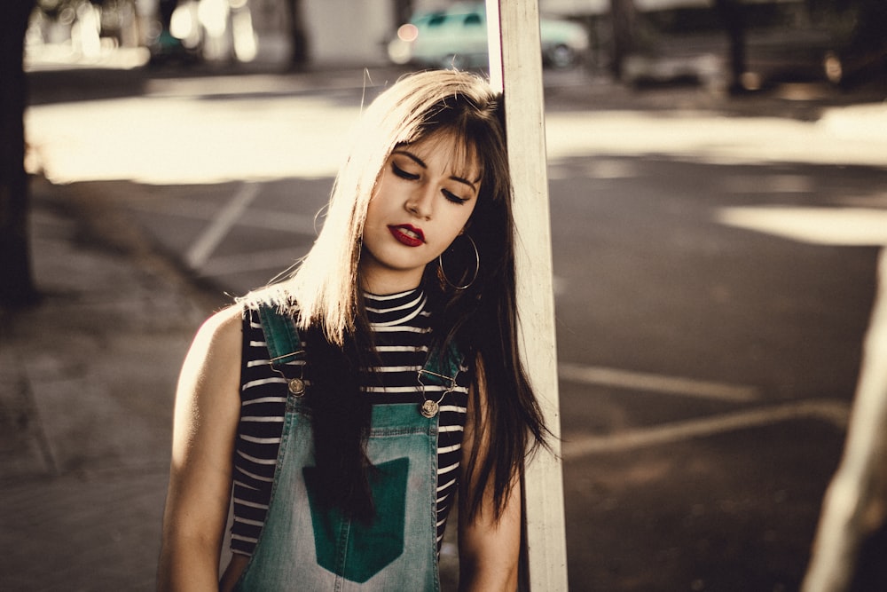 shallow focus photography of woman leaning on brown wooden post