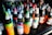 A collection of colorful ink bottles arranged closely together on a shelf. Each bottle has a twist cap, and they display a variety of bright labels with intricate designs. The inks include vibrant colors such as green, blue, red, and orange, indicating a diverse selection.