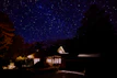 Evening shot of a bungalow lit warmly with surrounding trees and a starry sky