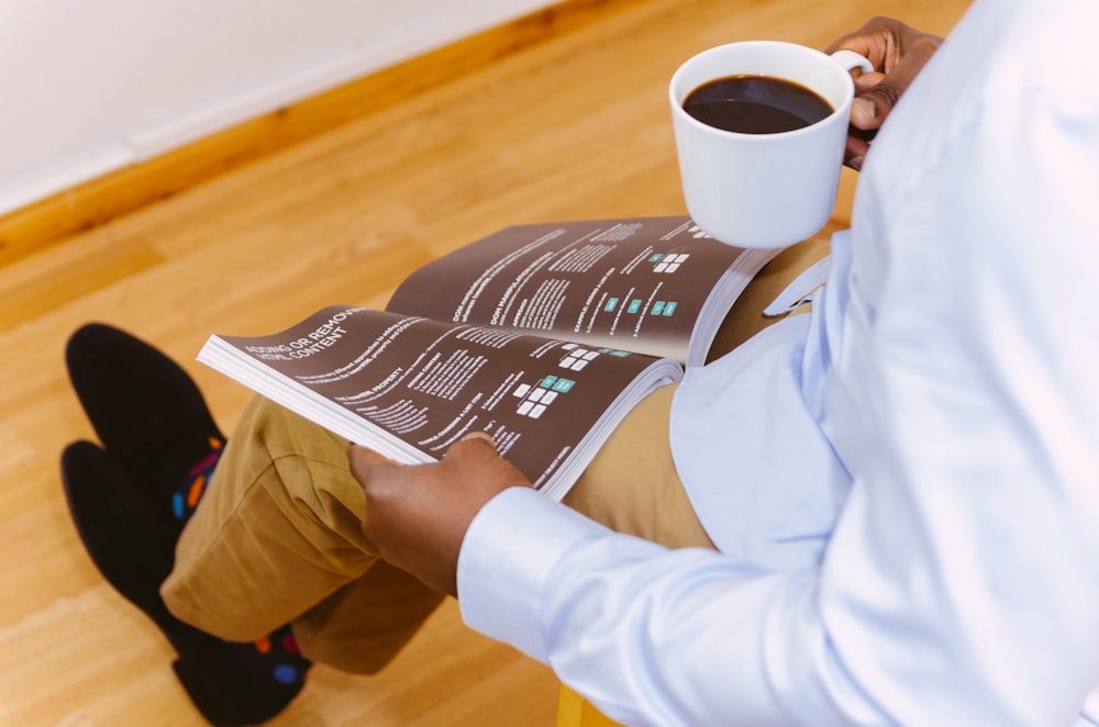 man holding coffee mug and reading magazine