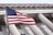 An American flag waves prominently in the foreground against a backdrop of a neoclassical building with large columns and intricate architectural details, conveying a sense of national pride.