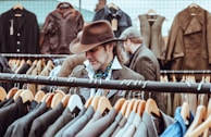 man in brown cowboy hat in front of hanged suit jackets
