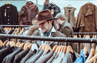 man in brown cowboy hat in front of hanged suit jackets
