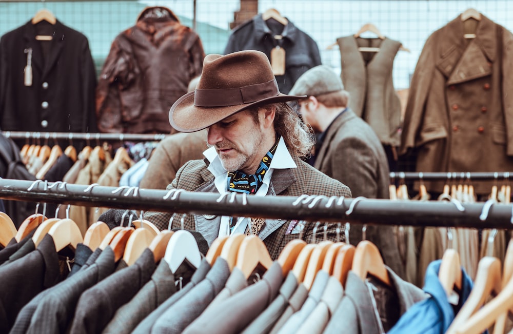 hombre con sombrero de vaquero marrón frente a chaquetas de traje colgadas